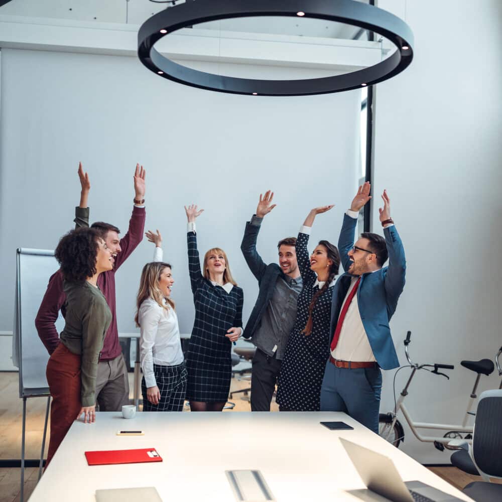 Vertical shot of a group of coworkers cheering in an office